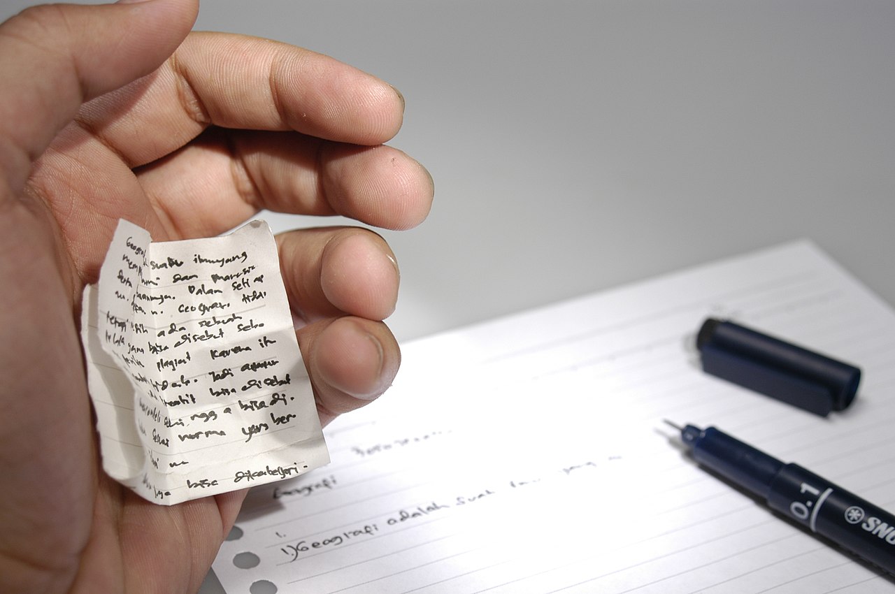 Someone writting an exam while with a small paper hidden on their hand